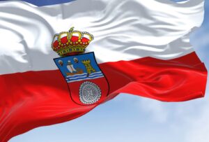 Una imagen de la bandera de Cantabria, bandera ondeando al viento con franjas horizontales blanca y roja, y un escudo con una corona en el centro.