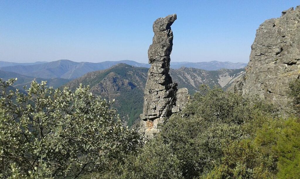 Monolito que sobresale entre la vegetación verde y densa de un paisaje montañoso.