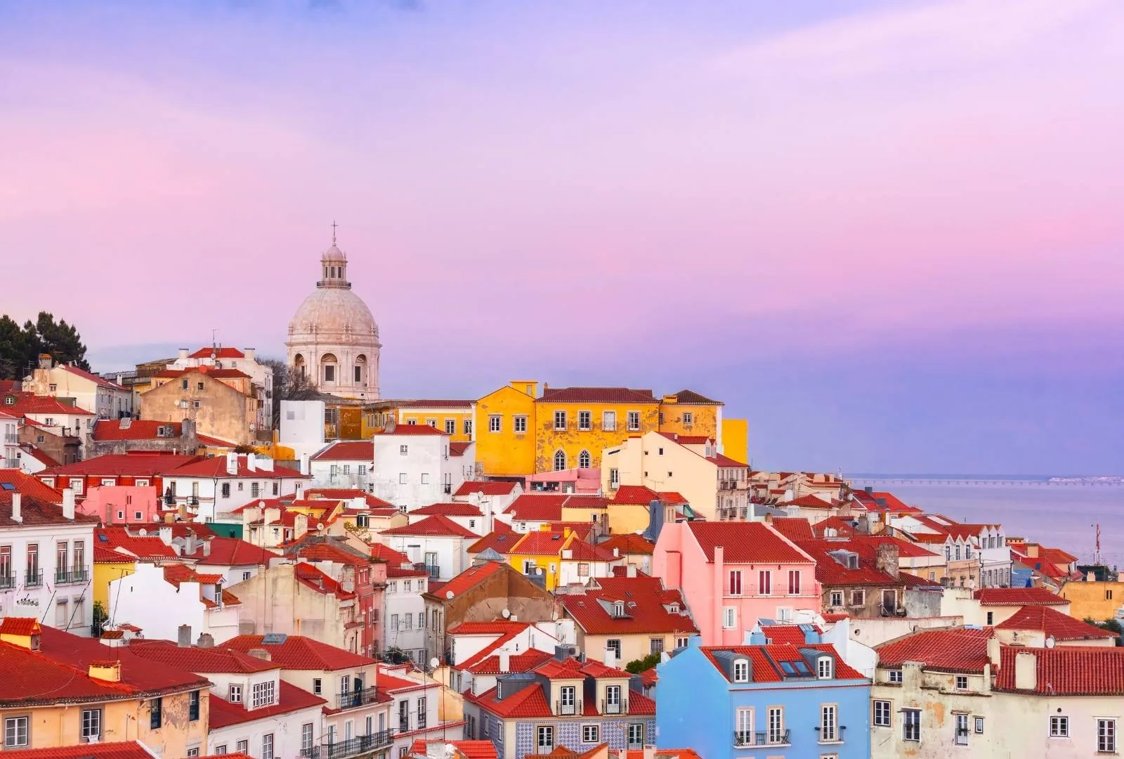 Vista panorámica de Alfama en Lisboa al atardecer, con casas de colores y el Panteón Nacional al fondo.