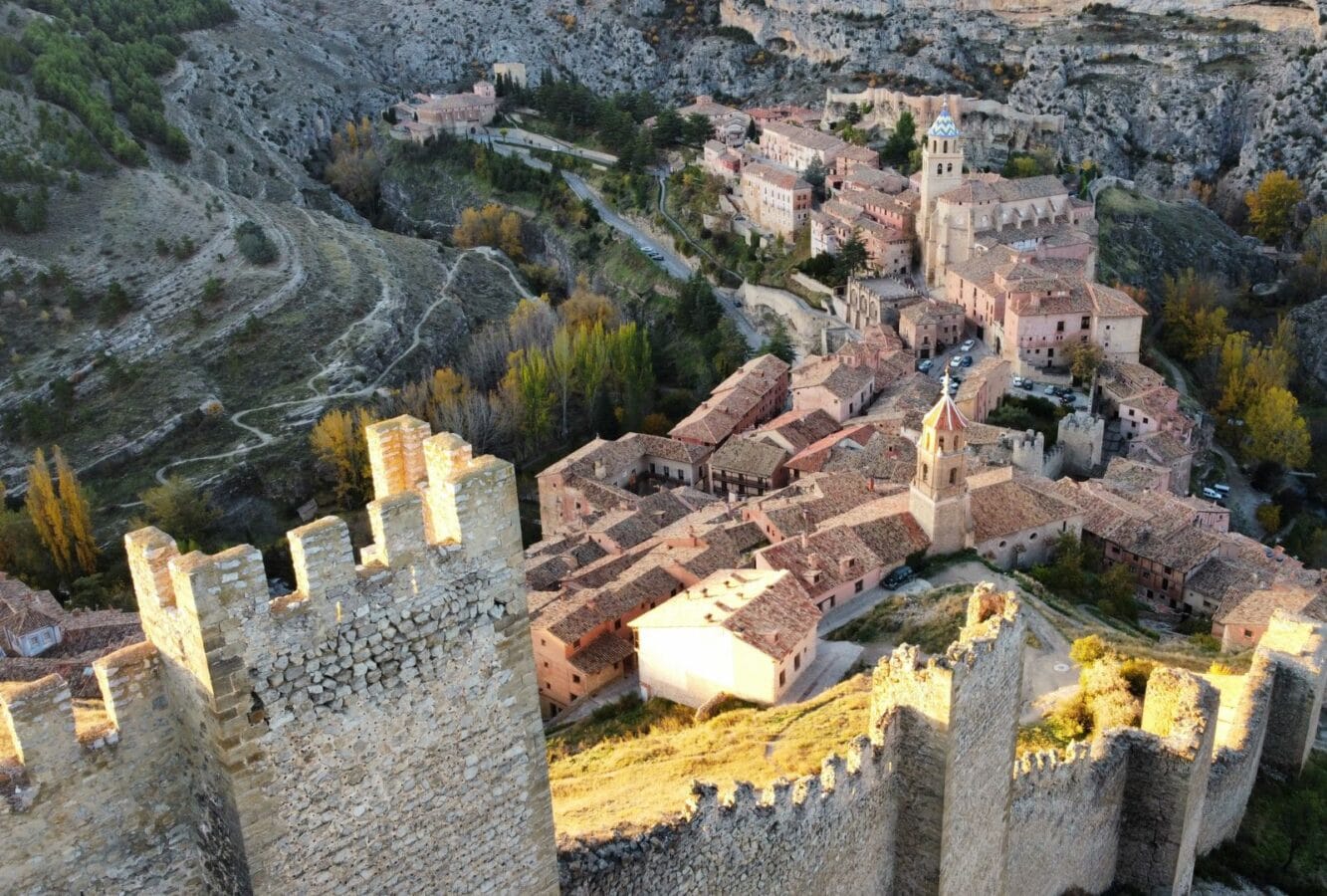 Vista aérea del pueblo de Albarracín, en Teruel, con sus murallas medievales y casas de piedra rojiza rodeadas de montañas.
