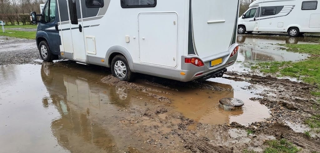 Autocaravana embarrada y atascada en un área de servicio inundada, con drenaje colapsado. Consecuencias de un mal mantenimiento o diseño del suelo.