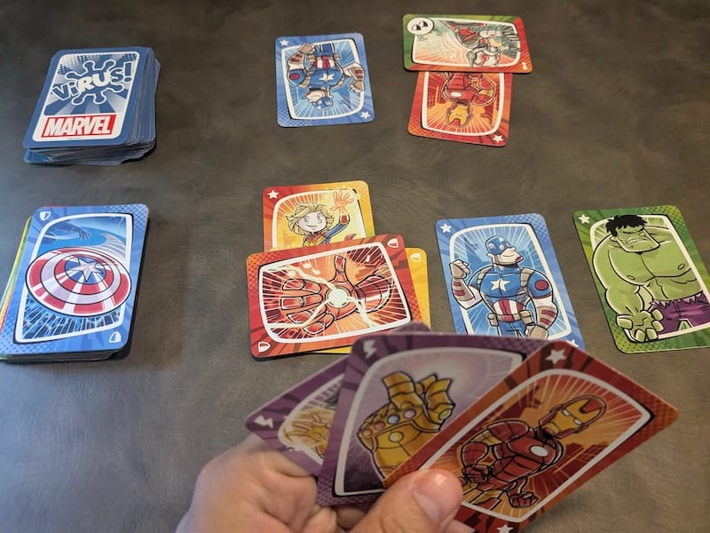 Cartas del juego Virus! Marvel con ilustraciones de superhéroes sobre una mesa camper.