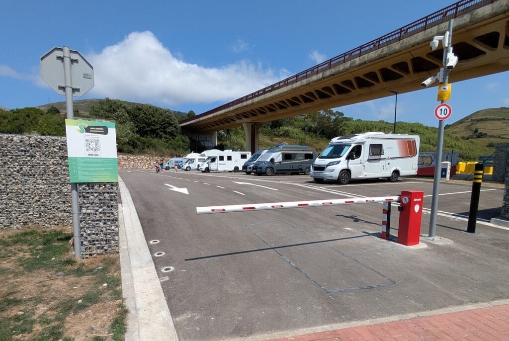 Vista de la entrada de La Arena Camper Park, con la barrera, cámaras de seguridad y autocaravanas al fondo.